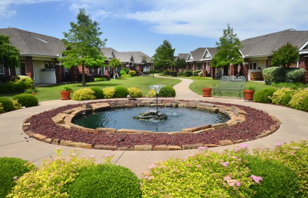A picturesque garden courtyard with a central fountain surrounded by lush greenery and buildings.