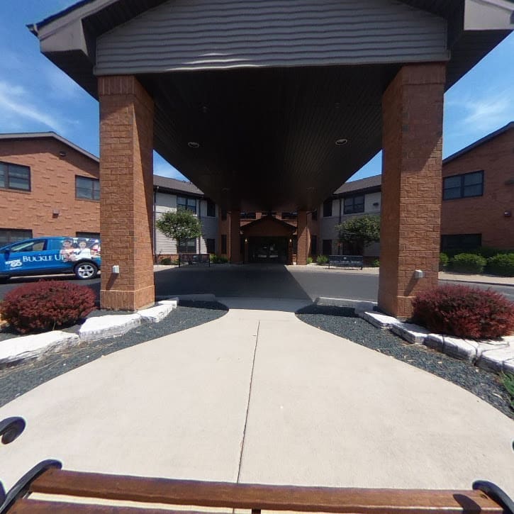 A building entrance featuring a covered walkway with columns and a paved path leading forward.