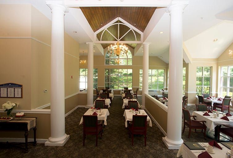 Elegant dining room with columns and a chandelier, featuring tables set for guests.