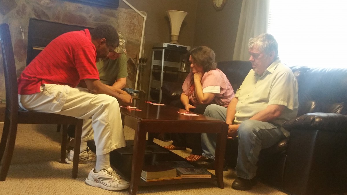 A group of people sits around a table in a living room, engaged in conversation.
