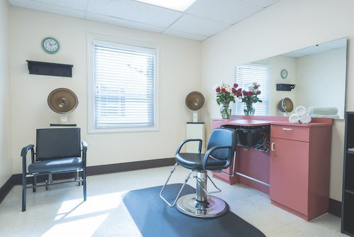 A well-lit hair salon interior with a styling chair and flowers on the counter.