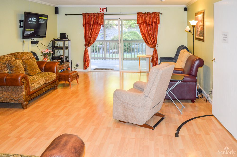 A spacious living room with comfortable seating and a television, featuring laminate flooring and large windows with red curtains.