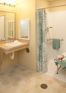 An accessible bathroom featuring a sink with a mirror, a shower with grab bars, and towels neatly placed.