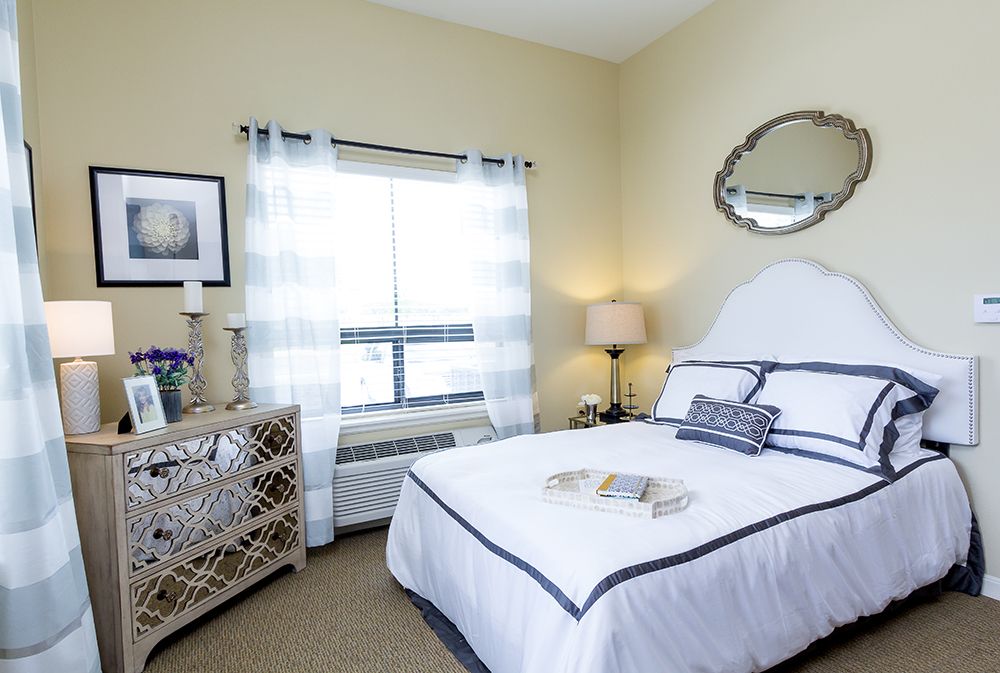 A cozy and minimalist bedroom with neutral tones, featuring a neatly made bed, a lamp on the bedside table, and light curtains covering the window.