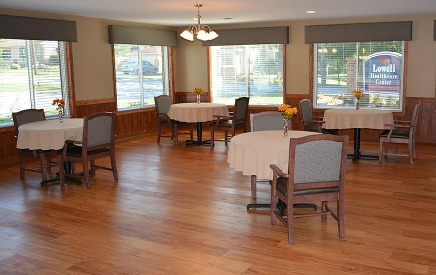 An empty dining room with several tables and chairs, featuring wooden floors and large windows.