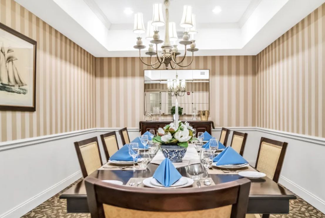 An elegantly set dining room table with blue napkins and a chandelier overhead.