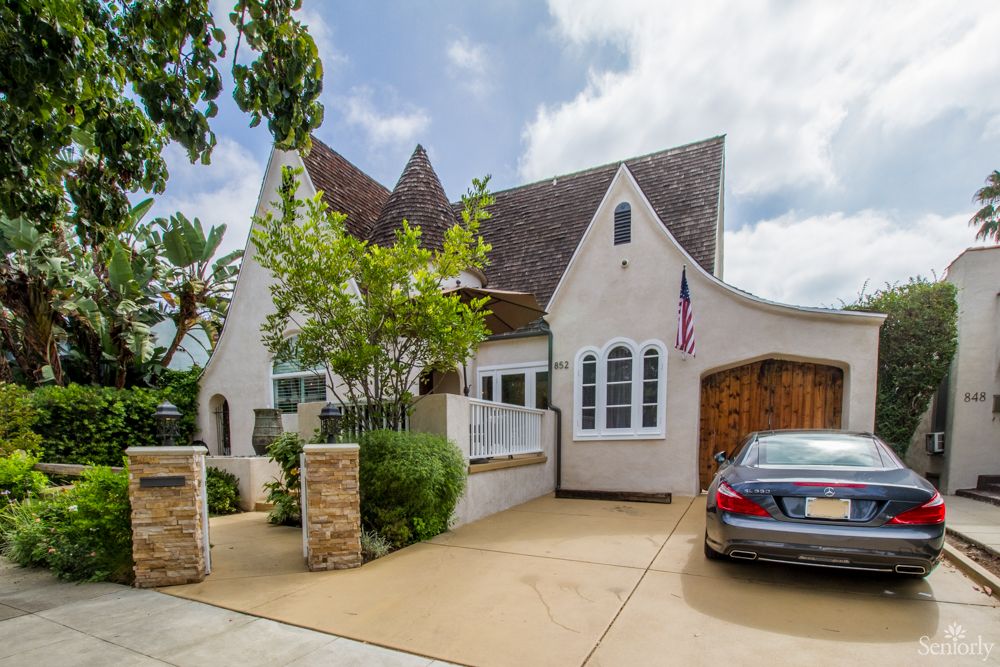 A charming house with a steep roof and an adjacent car in the driveway.