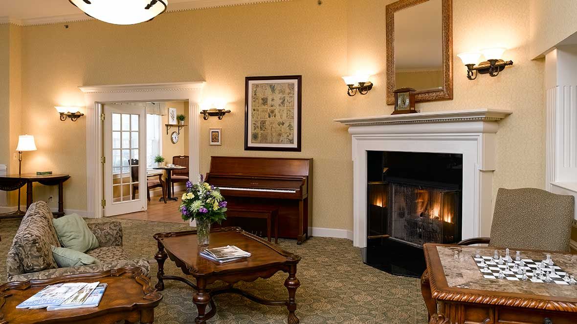 A cozy living room with a fireplace and piano, furnished in a traditional style.