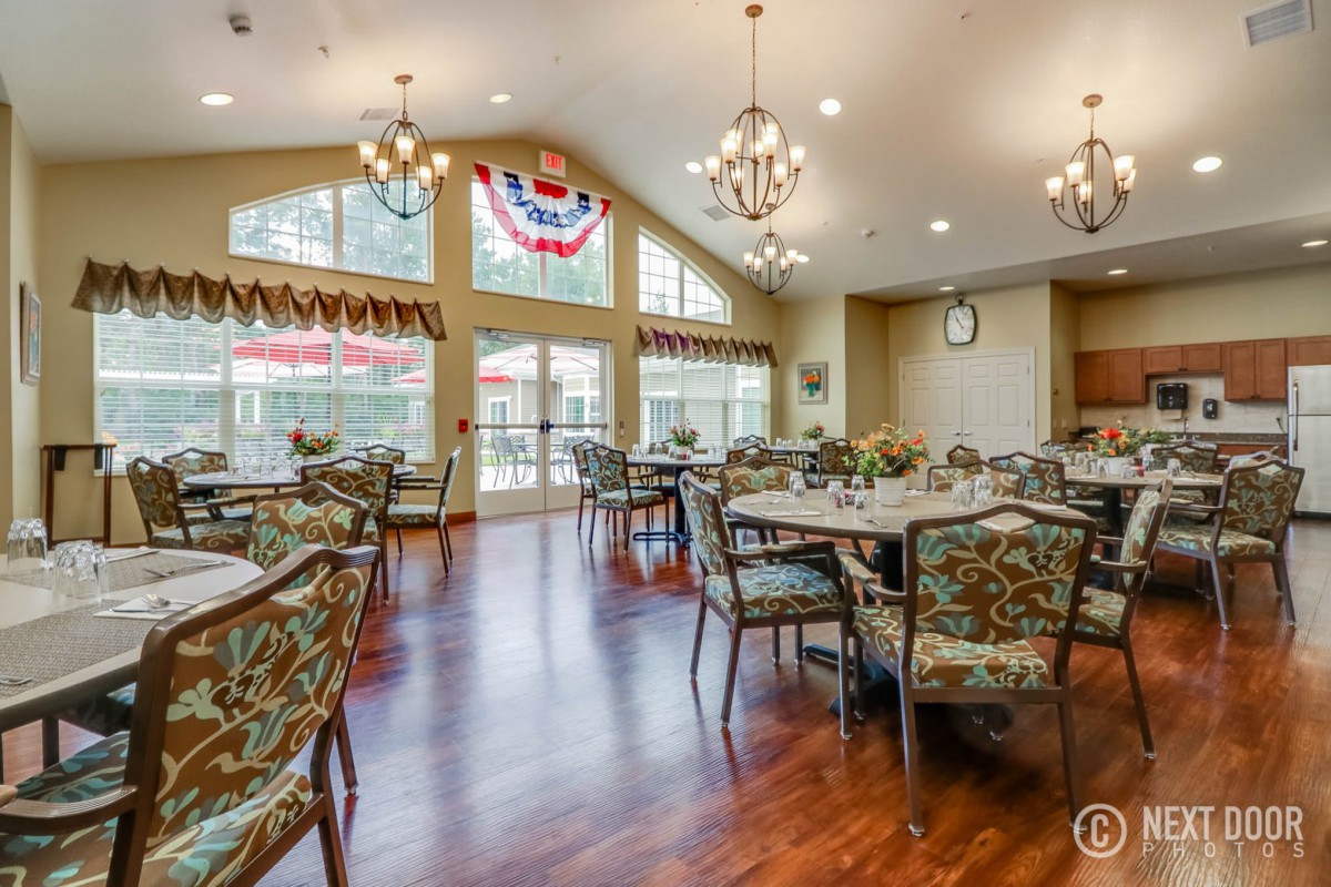 A spacious dining area with elegant chandeliers and large windows, featuring multiple tables and chairs.