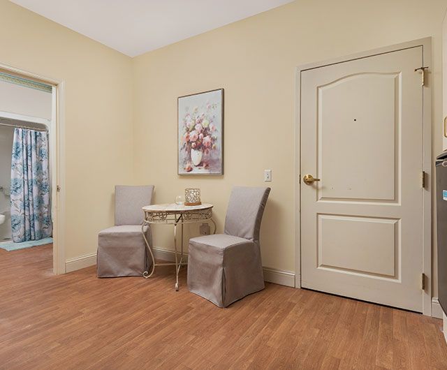 A cozy room interior with two chairs and a small table against a beige wall, decorated with a floral painting.