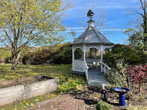 A charming gazebo situated in a serene garden, surrounded by lush greenery and a clear blue sky.