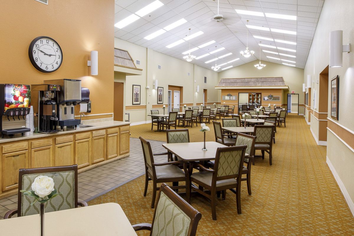 A spacious dining hall with neatly arranged tables and chairs, featuring bright overhead lighting.