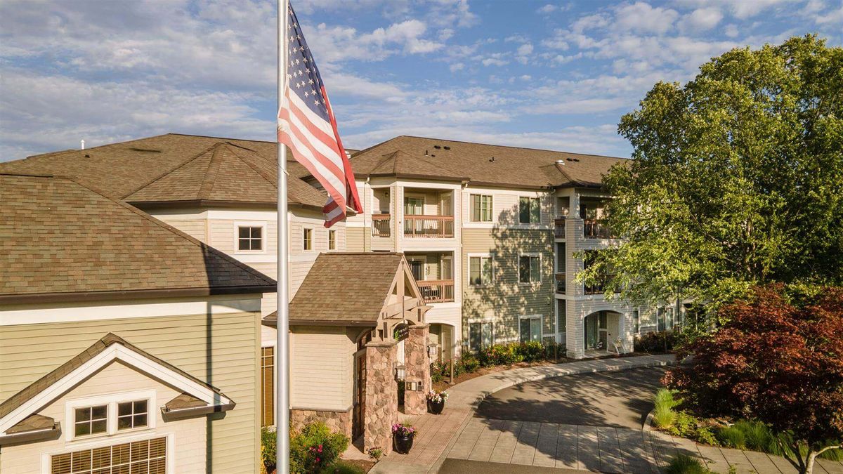 A residential apartment complex with an American flag in the foreground on a sunny day.