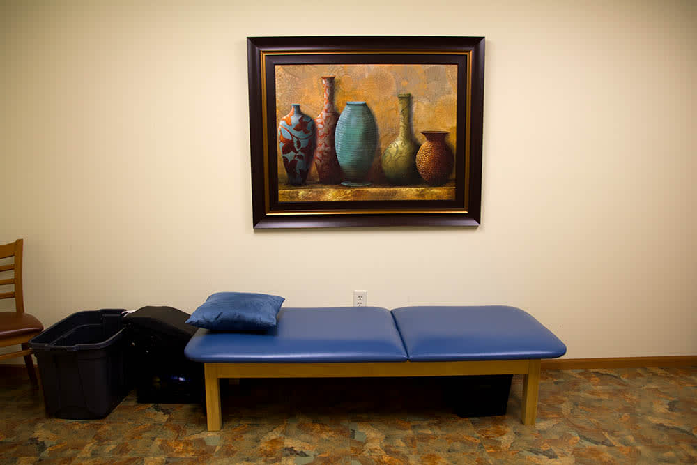 A therapy room with a treatment table and a painting on the wall.