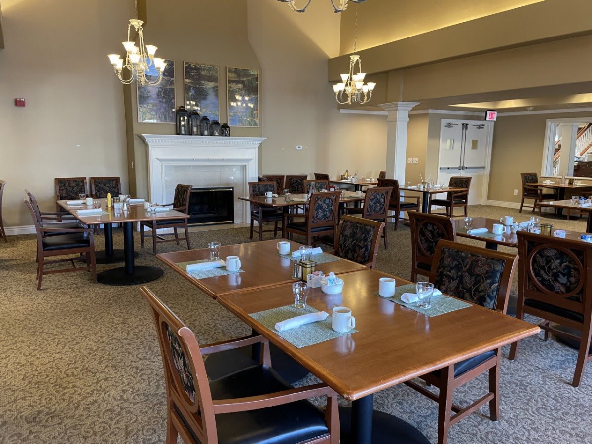 A cozy restaurant dining area with neatly arranged tables and chairs, featuring elegant chandeliers and a fireplace.