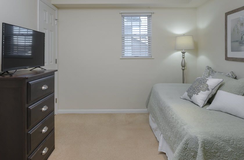 A cozy bedroom with a bed, lamp, and dresser.