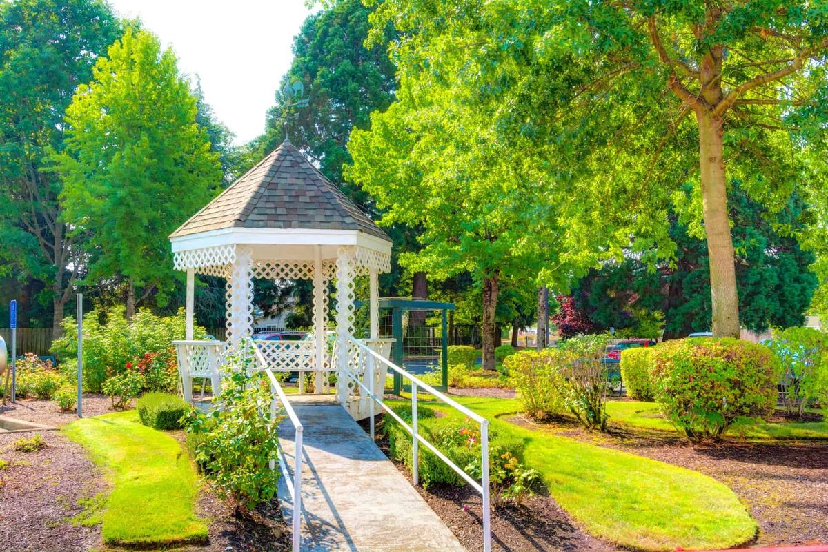A sunny day in a beautiful garden featuring a white gazebo surrounded by lush greenery.