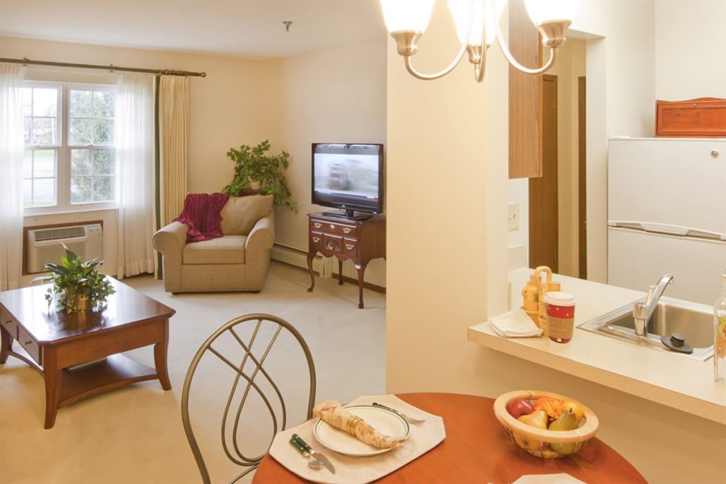 A cozy living and dining area with a comfortable armchair, TV, and a table set for two.