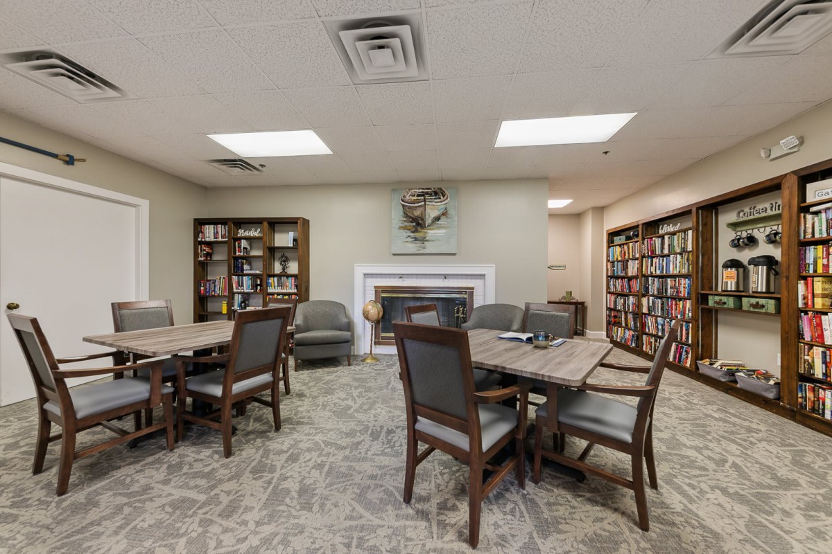 A cozy library room with tables, chairs, and shelves filled with books.