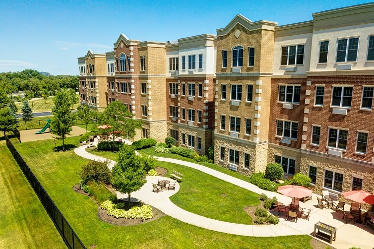A landscaped area with a pathway and outdoor seating in front of a multi-story apartment building.