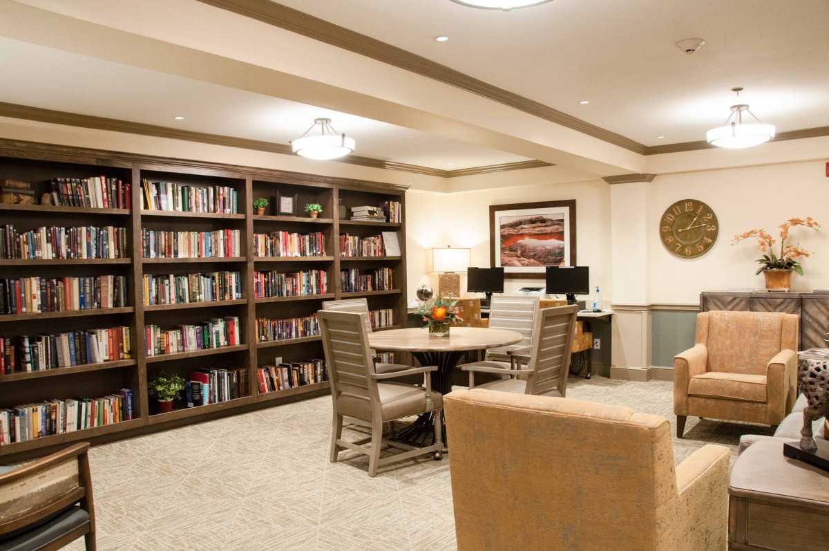 A cozy library space with bookshelves, tables, chairs, and computers.