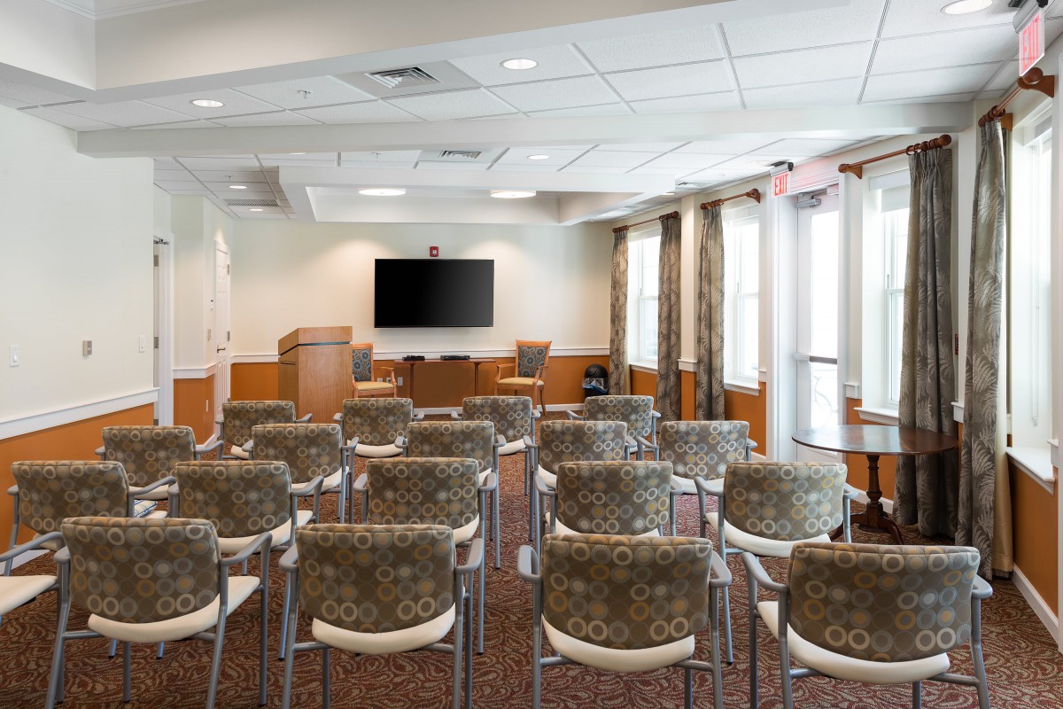An empty conference room with rows of chairs facing a large television screen and a podium.