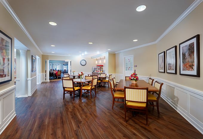 A spacious dining room with multiple tables and chairs, featuring wooden flooring and bright lighting.