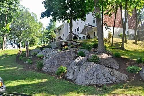 A house with a rock garden and trees on a sloped hill.