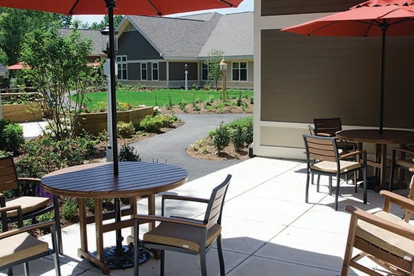 A sunny patio with tables and chairs under large umbrellas, overlooking a landscaped garden.
