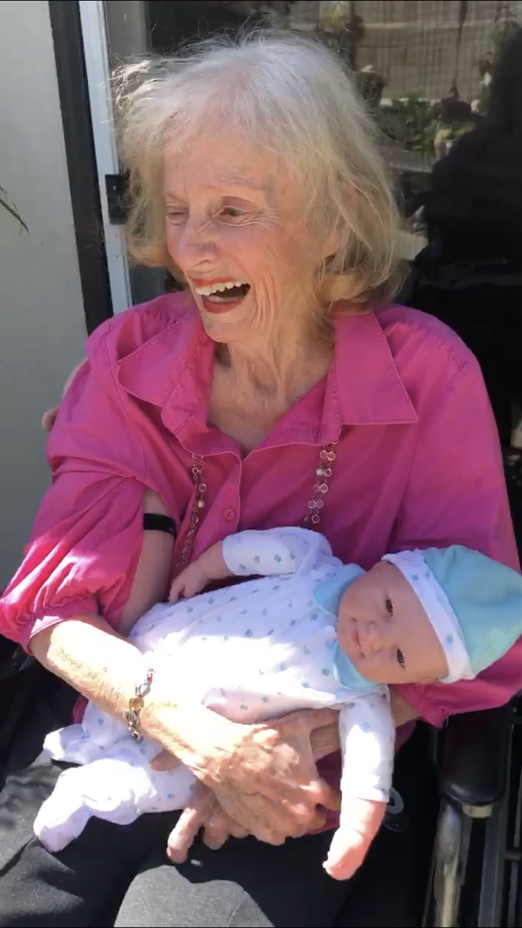 An elderly woman joyfully holds a baby while sitting outside.