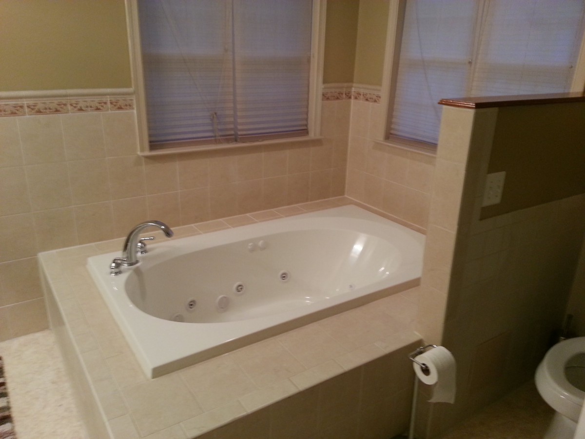 A tiled bathroom featuring a built-in bathtub and windows.
