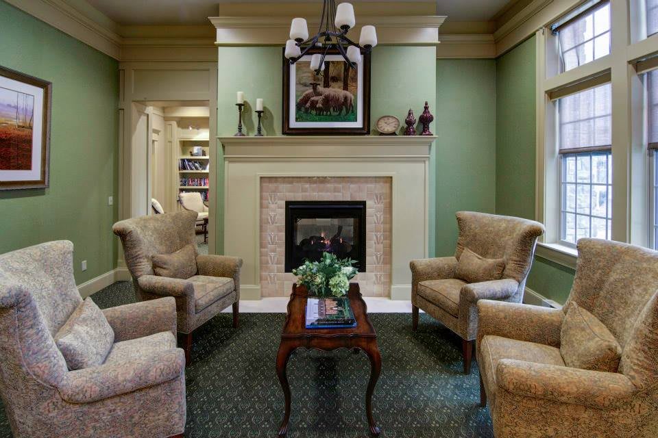 A cozy living room with a fireplace, surrounded by comfortable chairs and a small table.