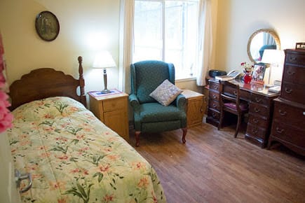 A cozy bedroom with a bed, armchair, and desk near a window.