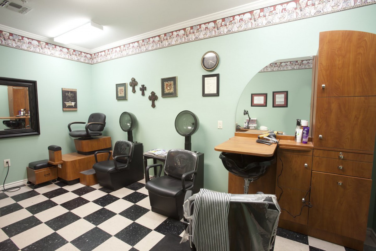 A cozy barber shop interior with chairs, mirrors, and hair dryers on a checkered floor.