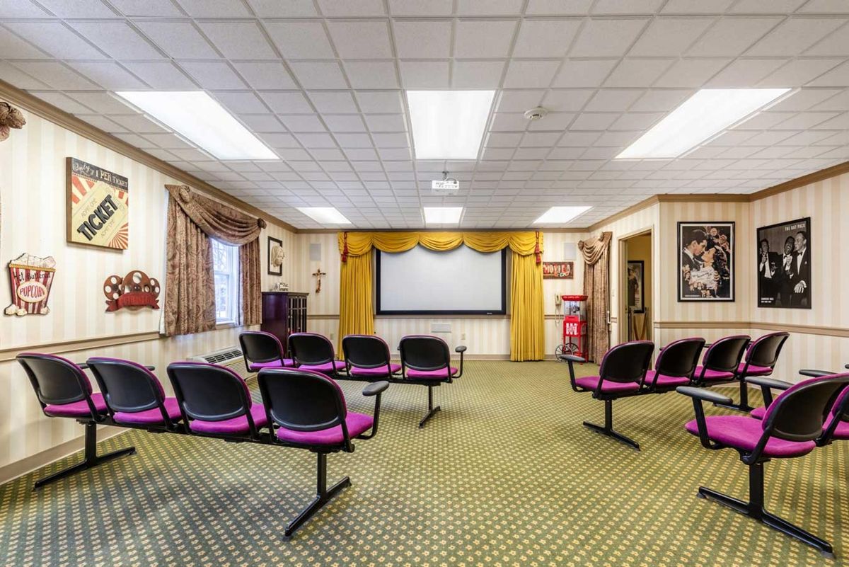 A conference room with rows of chairs facing a projector screen, decorated with curtains and framed posters.
