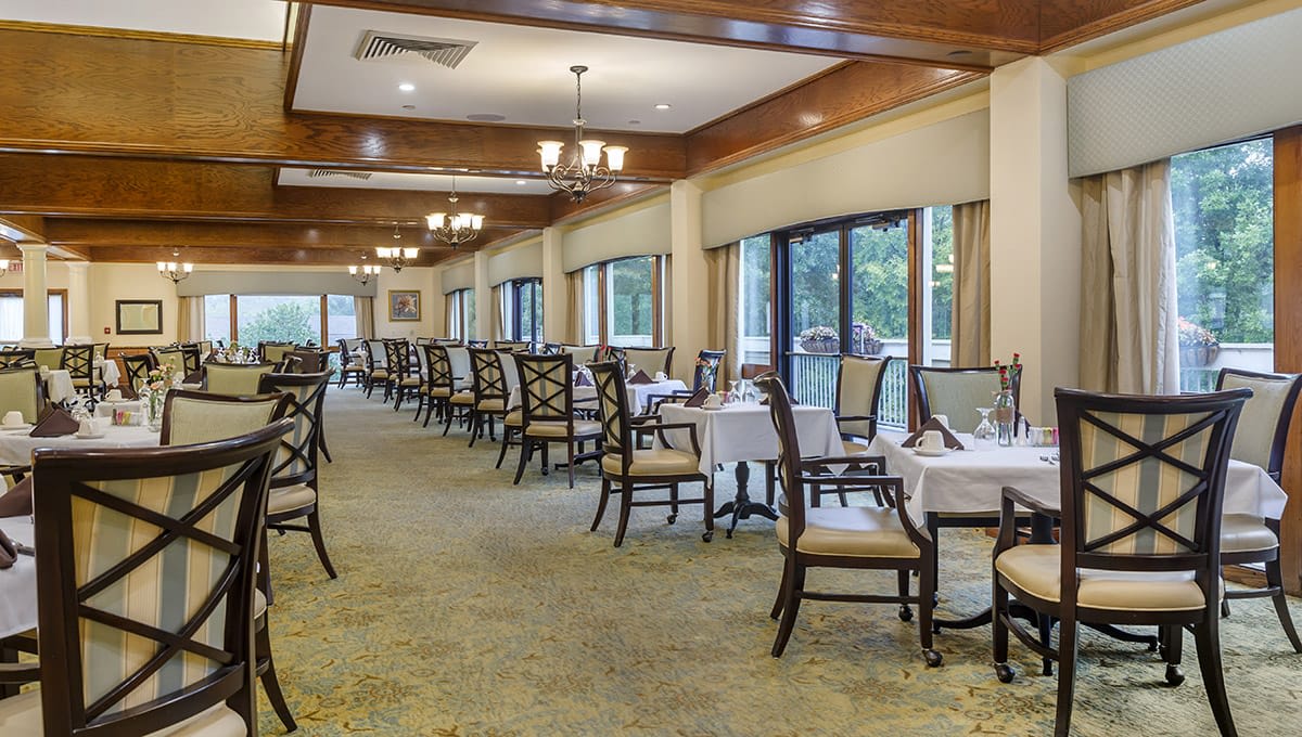 A spacious restaurant dining room with neatly arranged tables and chairs, featuring large windows and elegant decor.