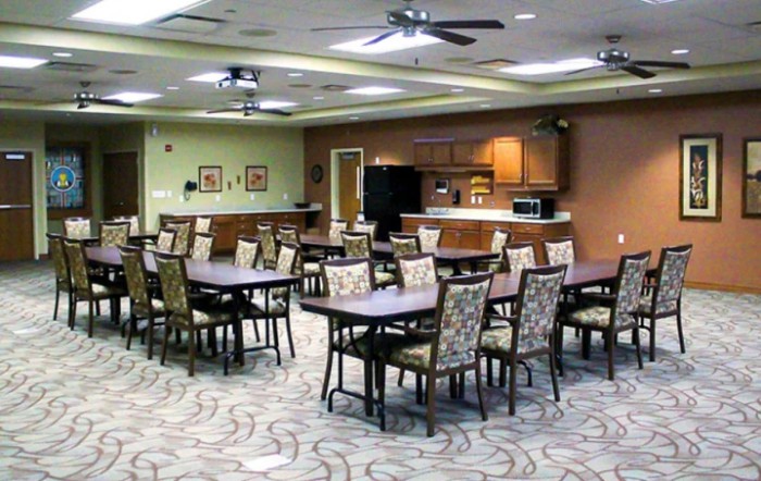 A spacious indoor dining area with multiple tables and chairs, featuring ceiling fans and a carpeted floor.