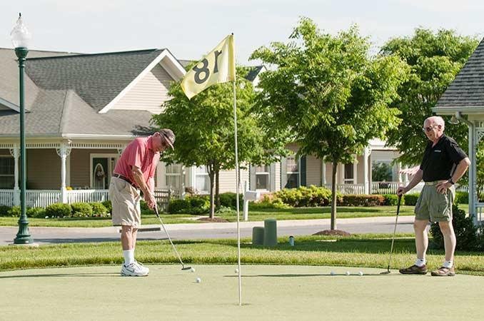 A person playing golf on a putting green in a residential neighborhood.