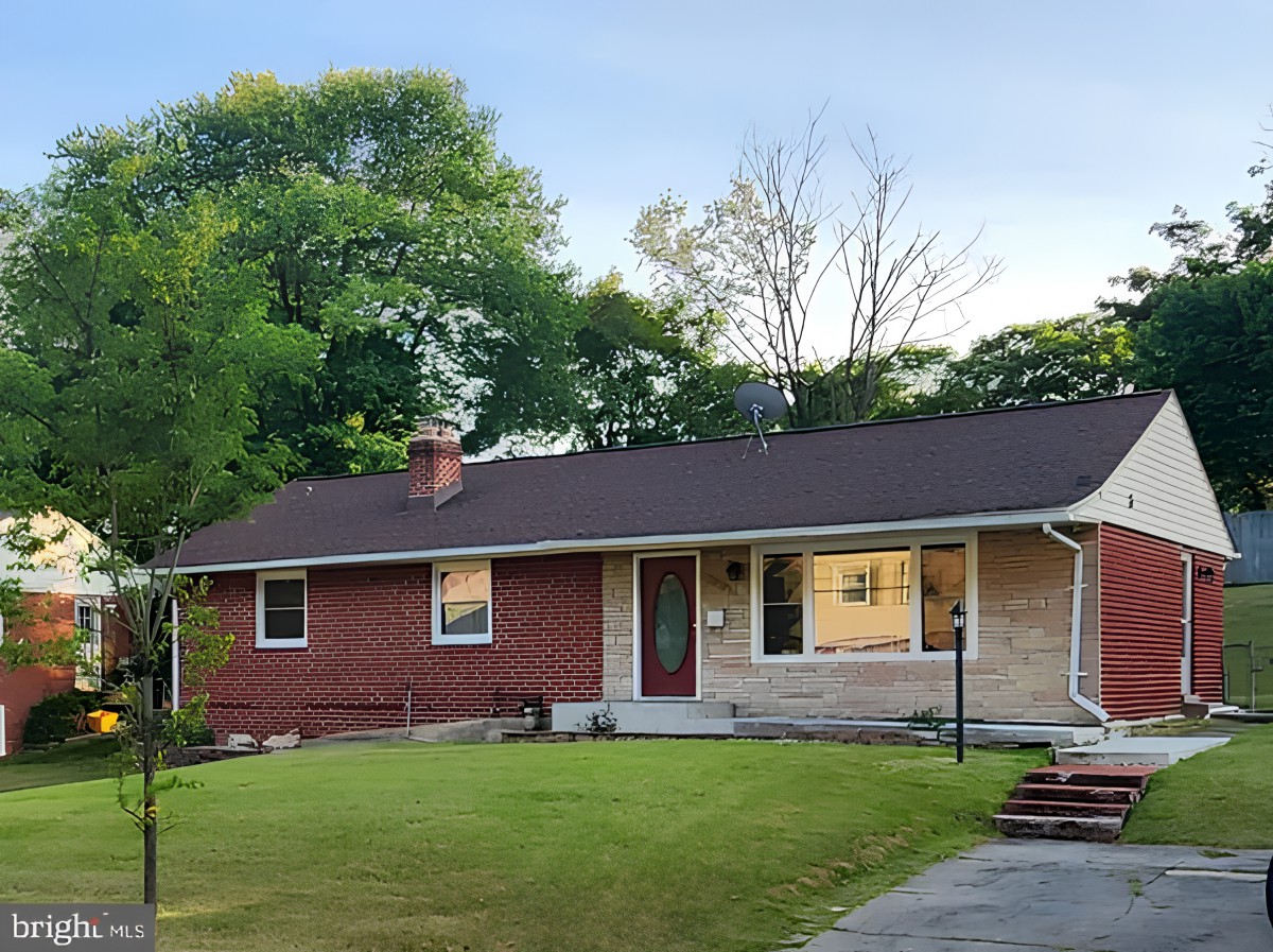 A suburban single-story house with a well-kept yard and surrounding trees.