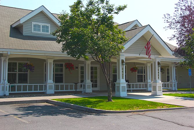 A quaint house with a front porch and an American flag, surrounded by trees.