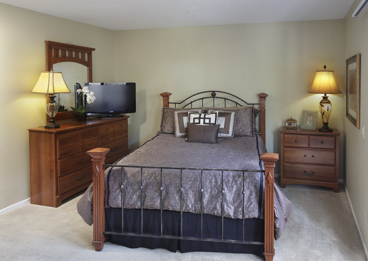 A cozy bedroom with a metal-framed bed, wooden dresser, and a TV.