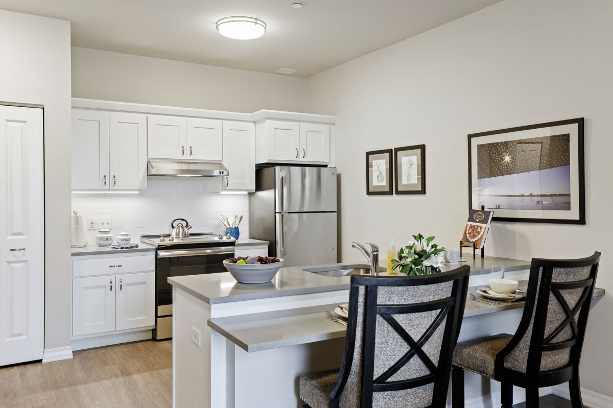 A modern kitchen with white cabinets and stainless steel appliances, featuring a small dining area with a countertop.