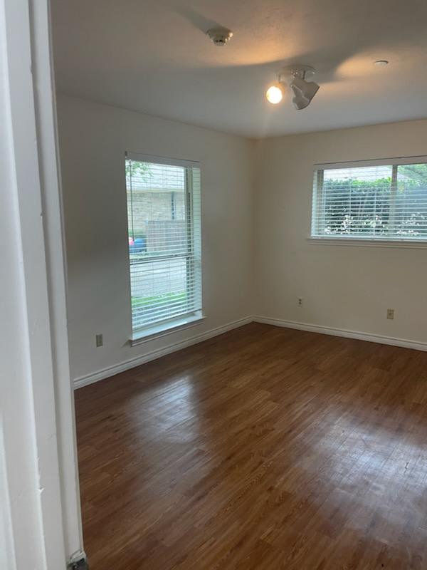 An empty room with hardwood floors and large windows letting in natural light.