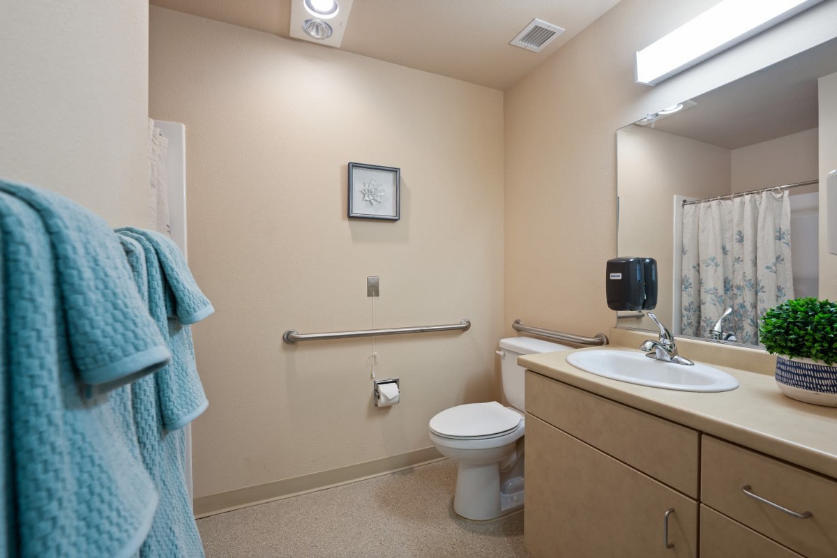 A clean and accessible bathroom with a toilet, grab bar, sink, and mirror.