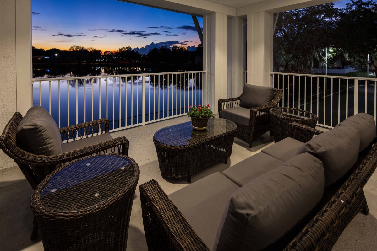 A cozy balcony overlooking a tranquil lake at sunset, furnished with comfortable rattan seating.