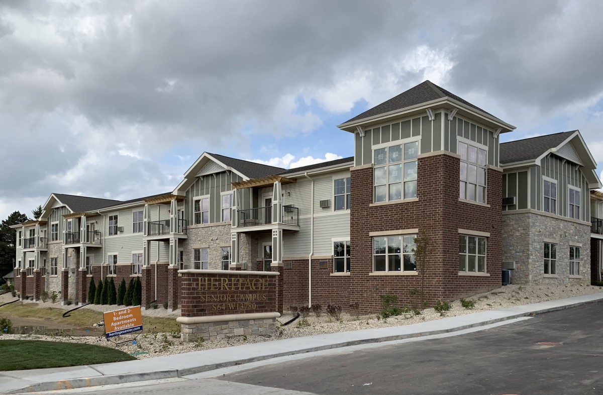 A modern two-story apartment building with a brick facade under a cloudy sky.