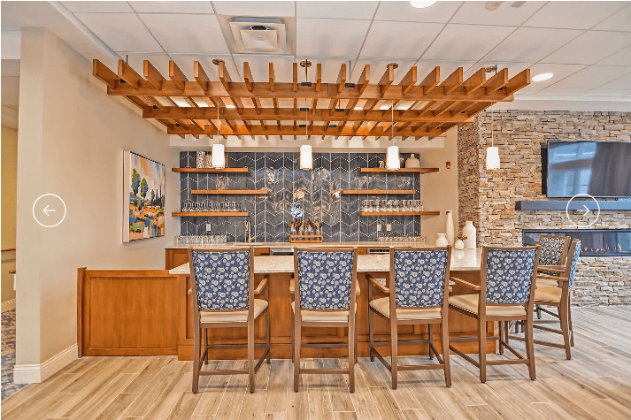 A modern bar interior featuring a wooden counter with stools, pendant lights, and a stone accent wall.