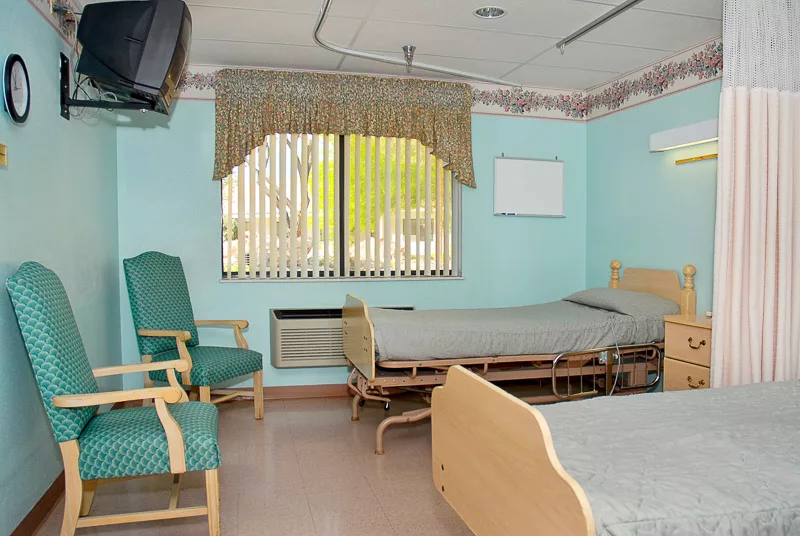 A hospital room with two beds, a window, and a television mounted on the wall.