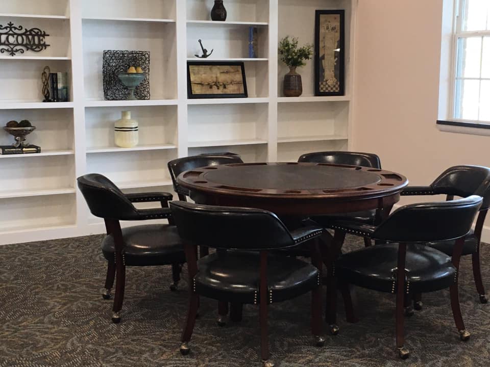 A cozy room with a round wooden table surrounded by chairs, featuring a decorative bookshelf in the background.
