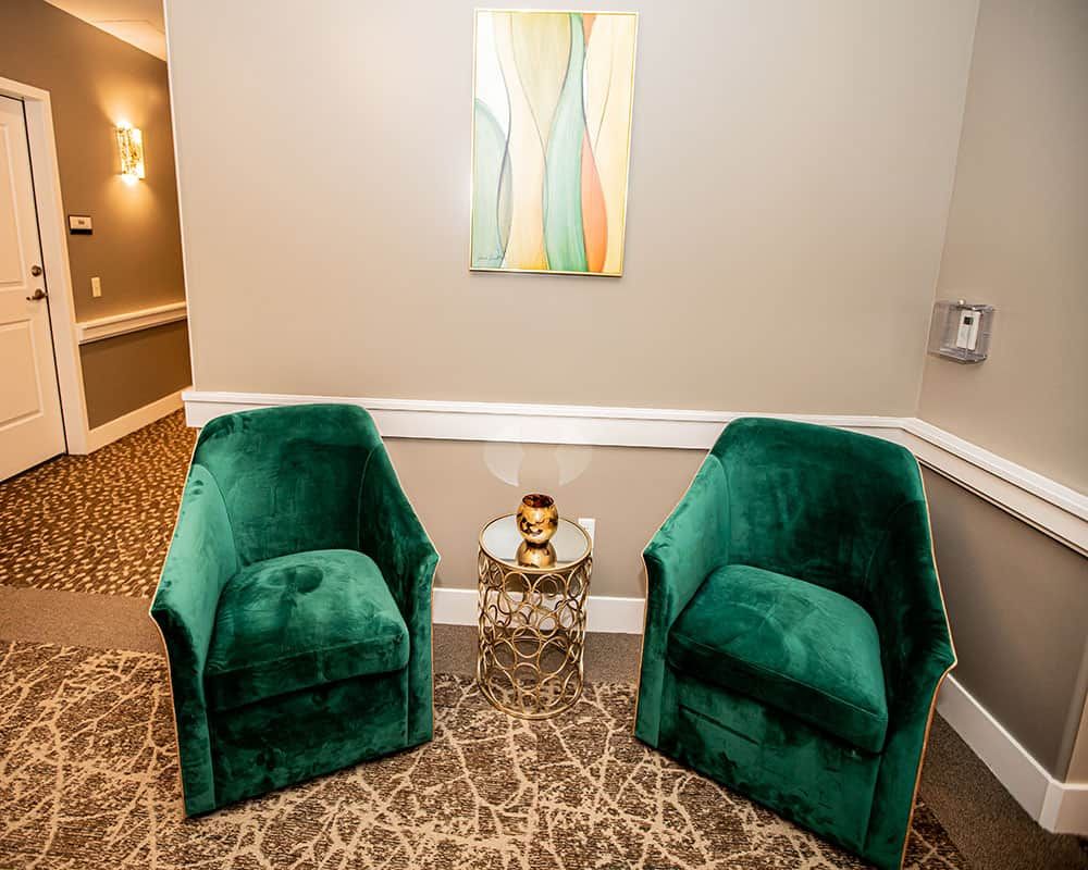 A cozy seating area with two green chairs and a small side table in a hallway.